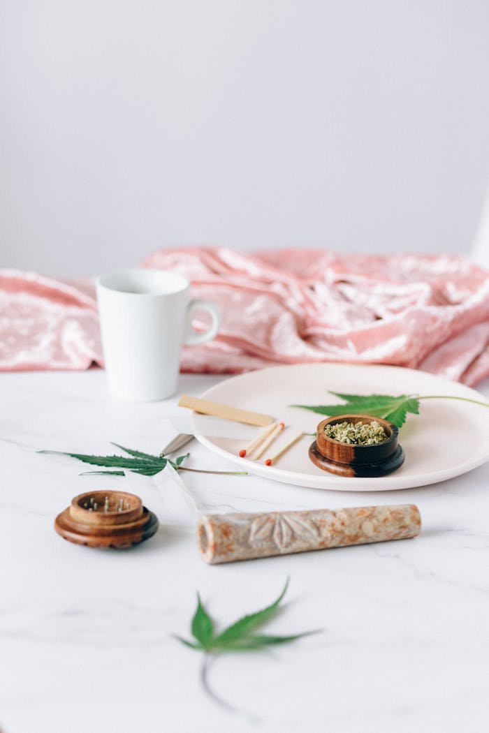 Artistic still life featuring cannabis leaf, cup, and rolling papers on a white table.